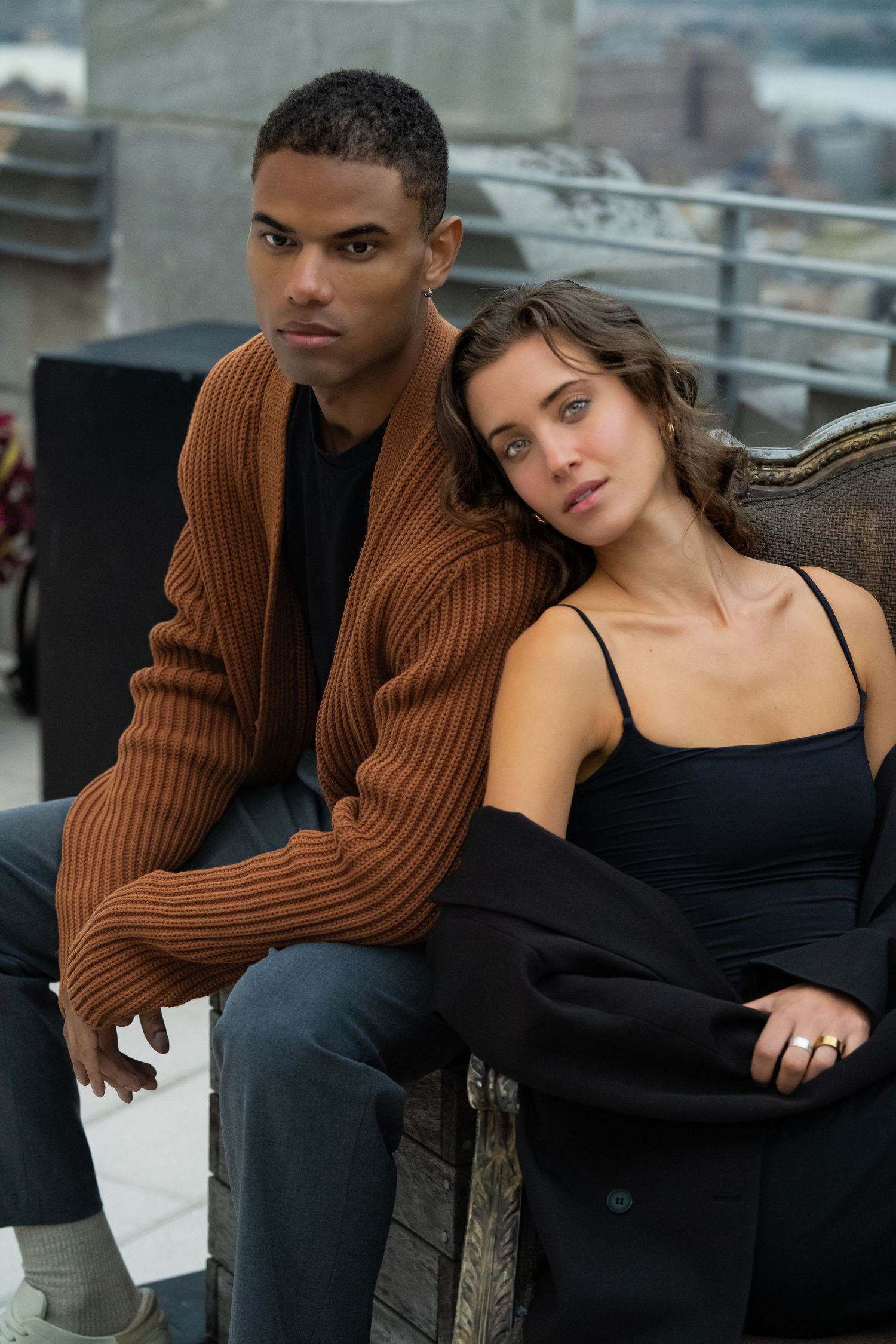 Romantic rooftop scene with couple in brown sweater and black outfit.