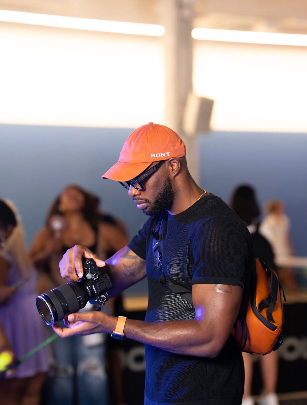 Professional photographer wearing an orange cap and navy shirt takes photos with a DSLR camera in multiple poses.