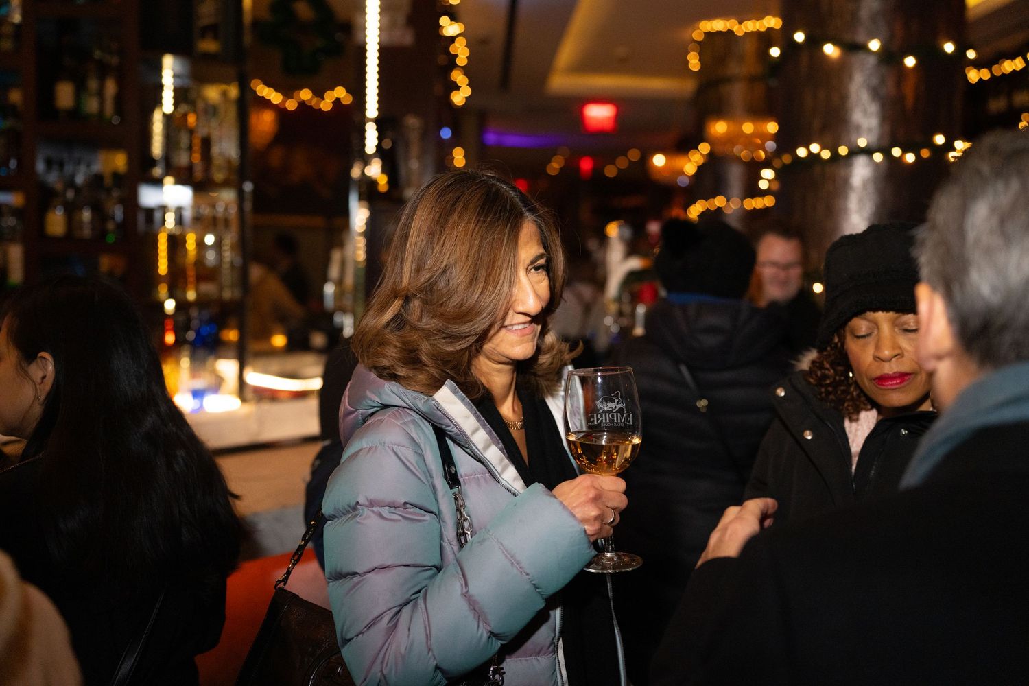 People enjoying a nighttime social gathering with string lights and warm ambiance in the background.