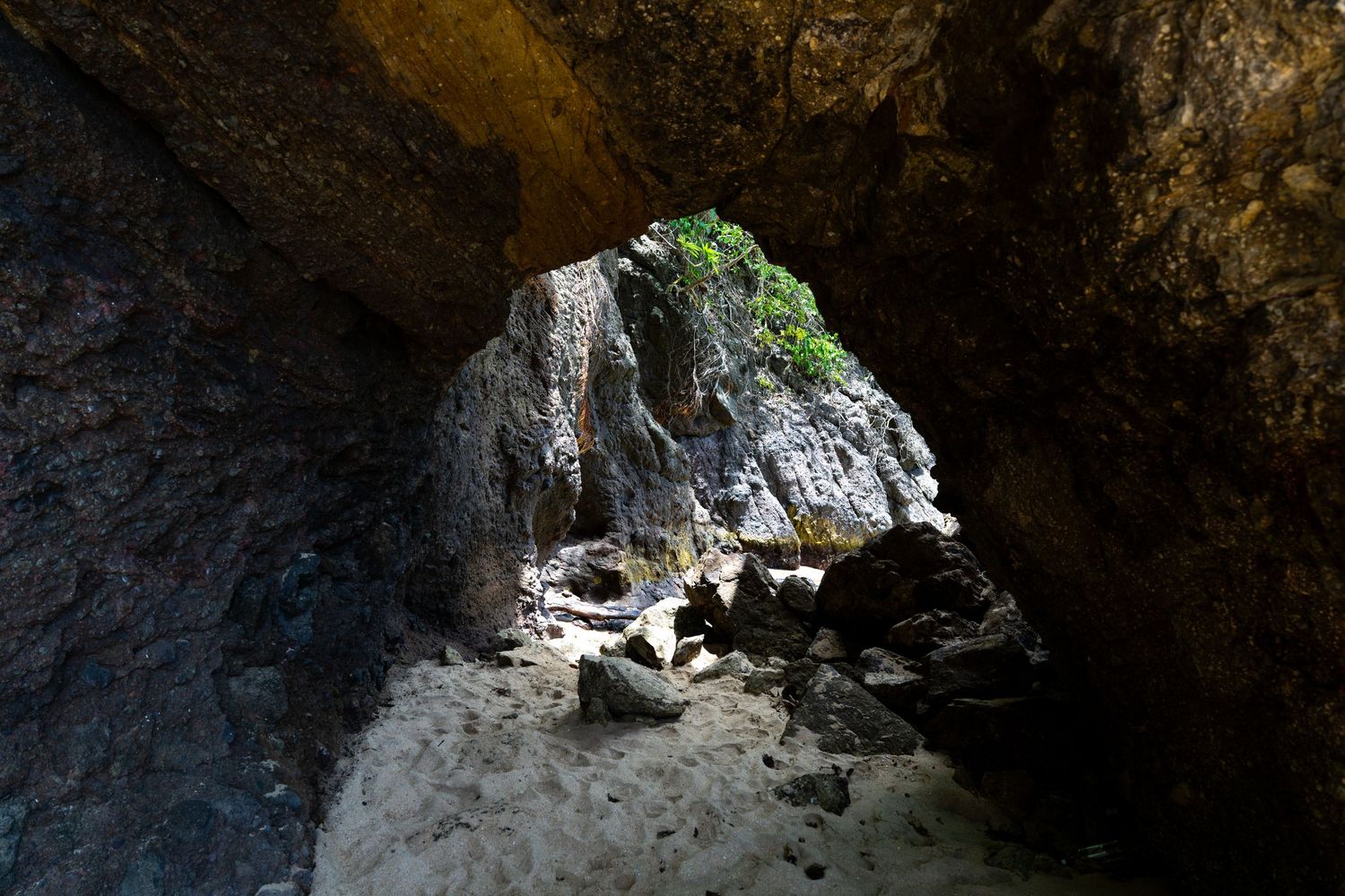 Natural cave opening with sunlight streaming through, creating dramatic lighting on limestone walls.