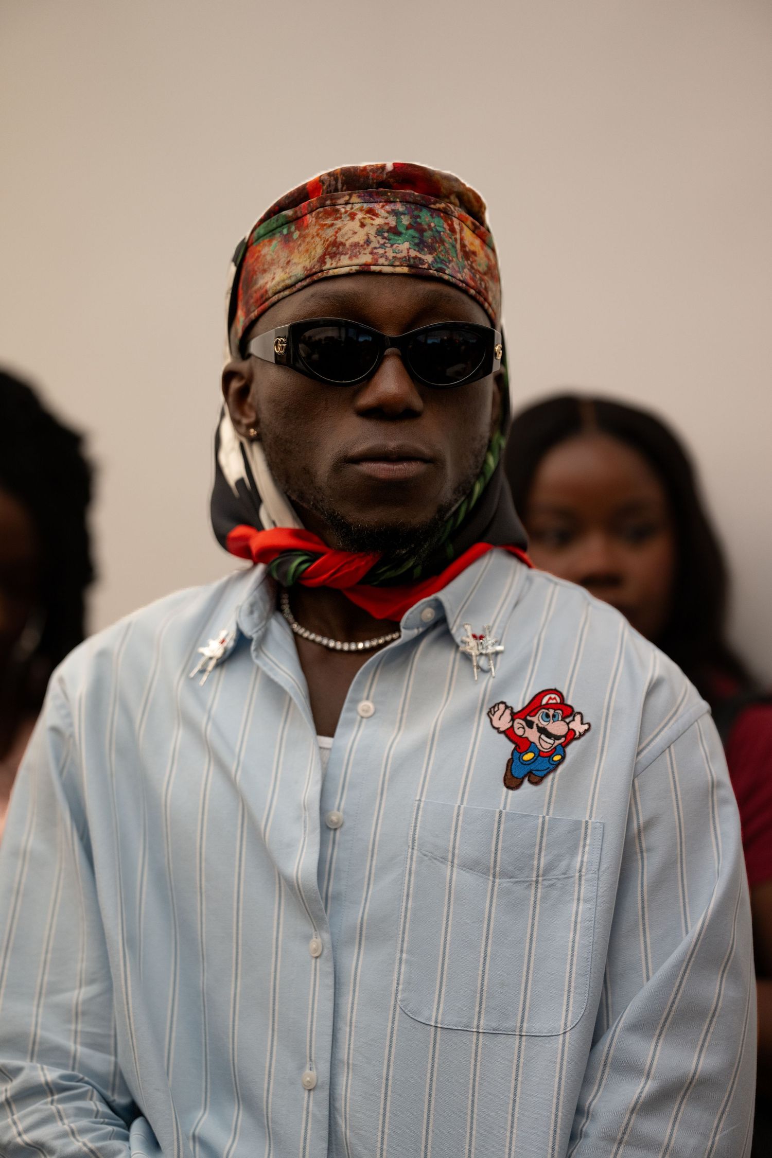 Person wearing striped white shirt and patterned bandana with sunglasses in indoor setting.