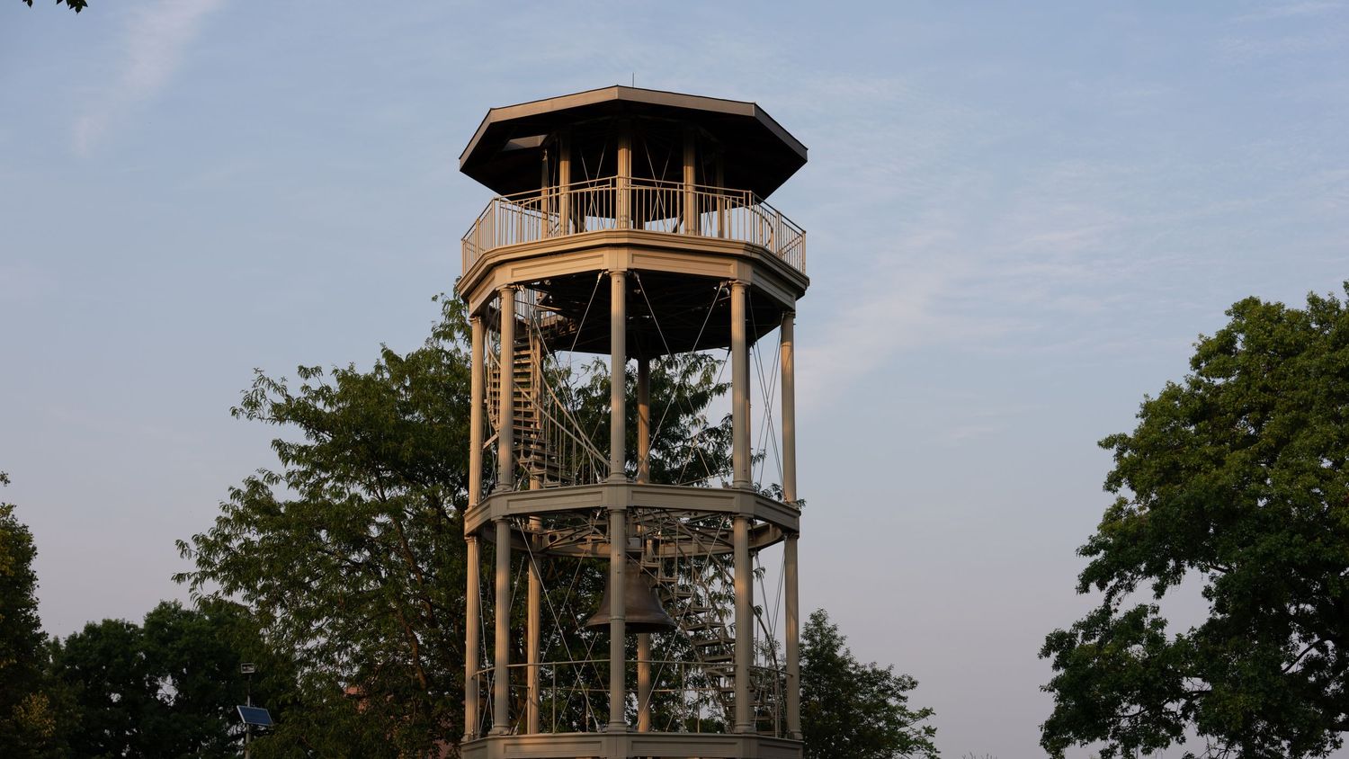 Tall wooden observation tower with octagonal platform surrounded by trees against a clear evening sky.