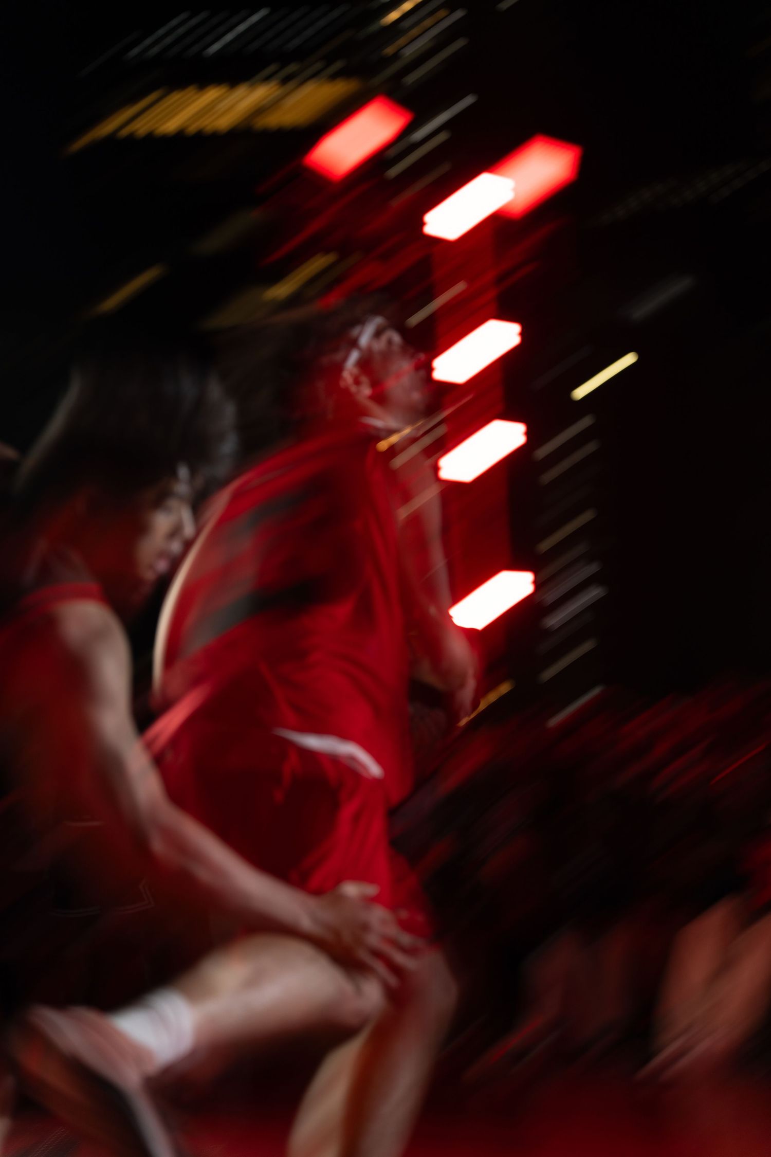 Motion-blurred athletes performing under dramatic red stage lighting.