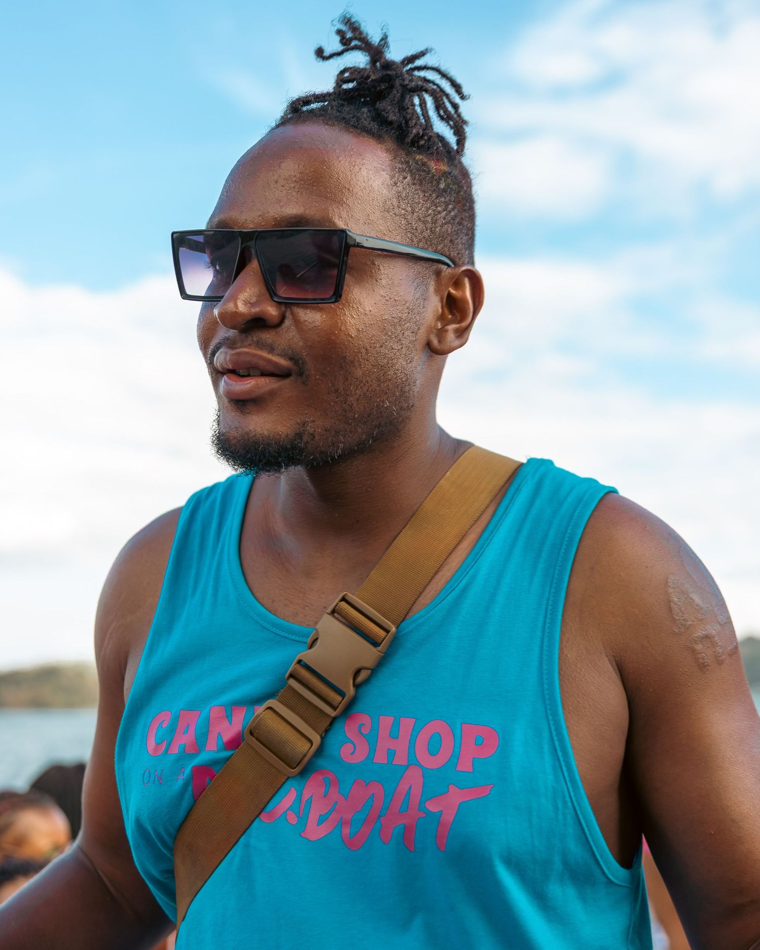 Person wearing turquoise tank top with text and sunglasses against blue sky background.