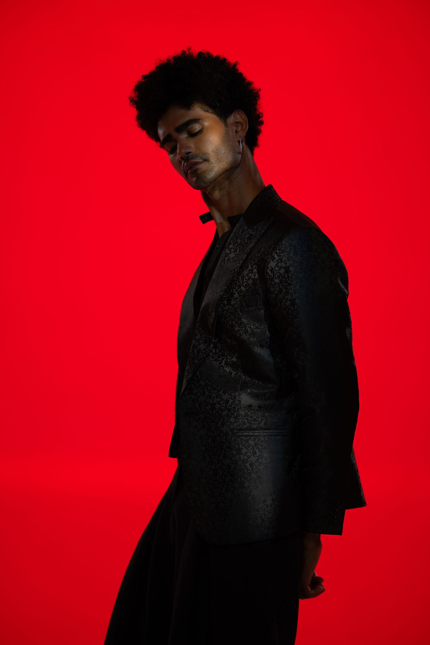 Dramatic silhouette portrait against vibrant red background wearing dark clothing.