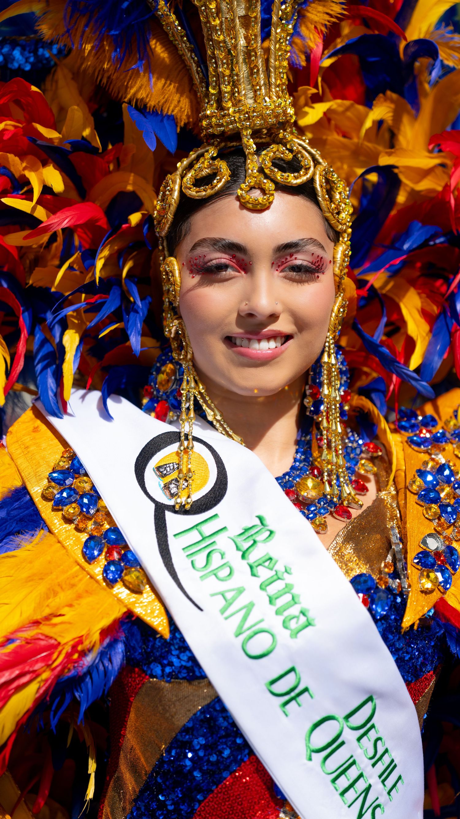 A festival participant wearing an ornate gold headdress and colorful decorations smiles brightly.
