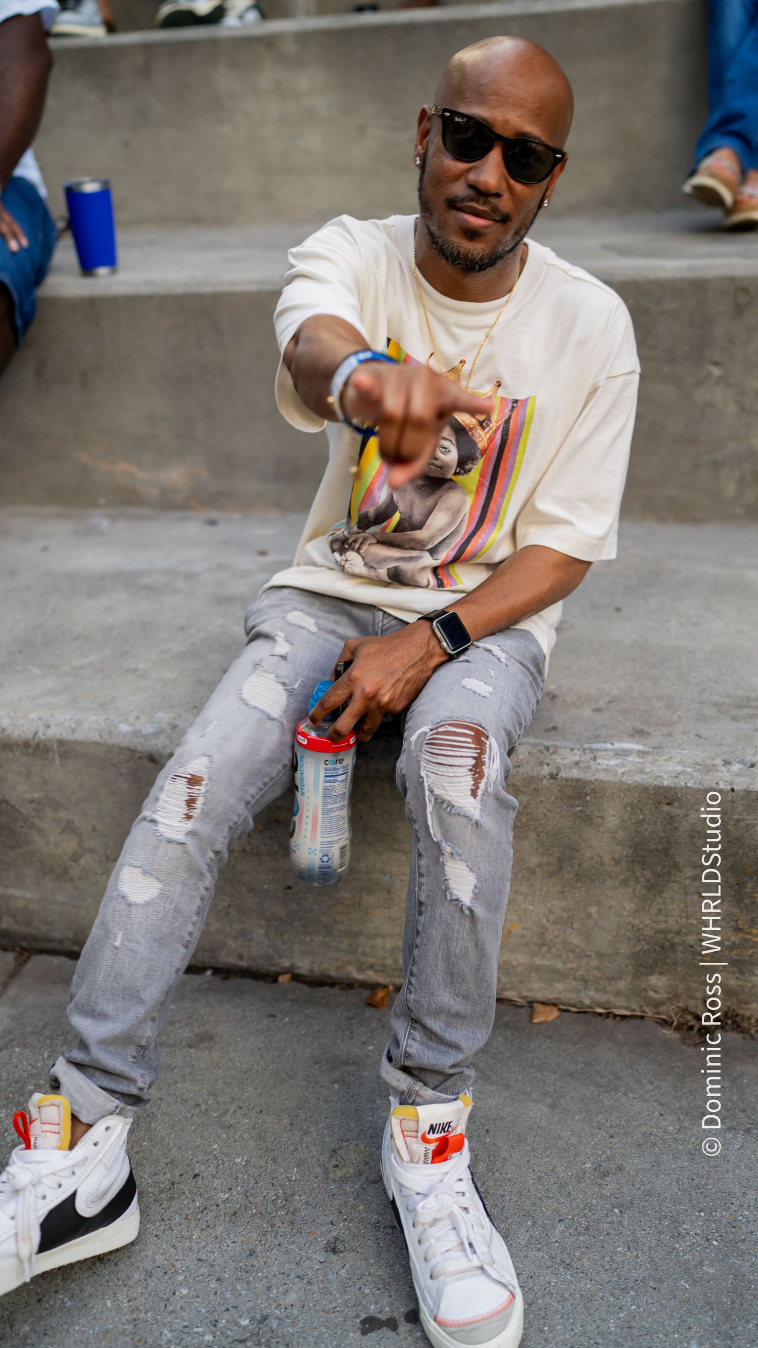 Person in distressed jeans and white sneakers sitting on concrete steps.