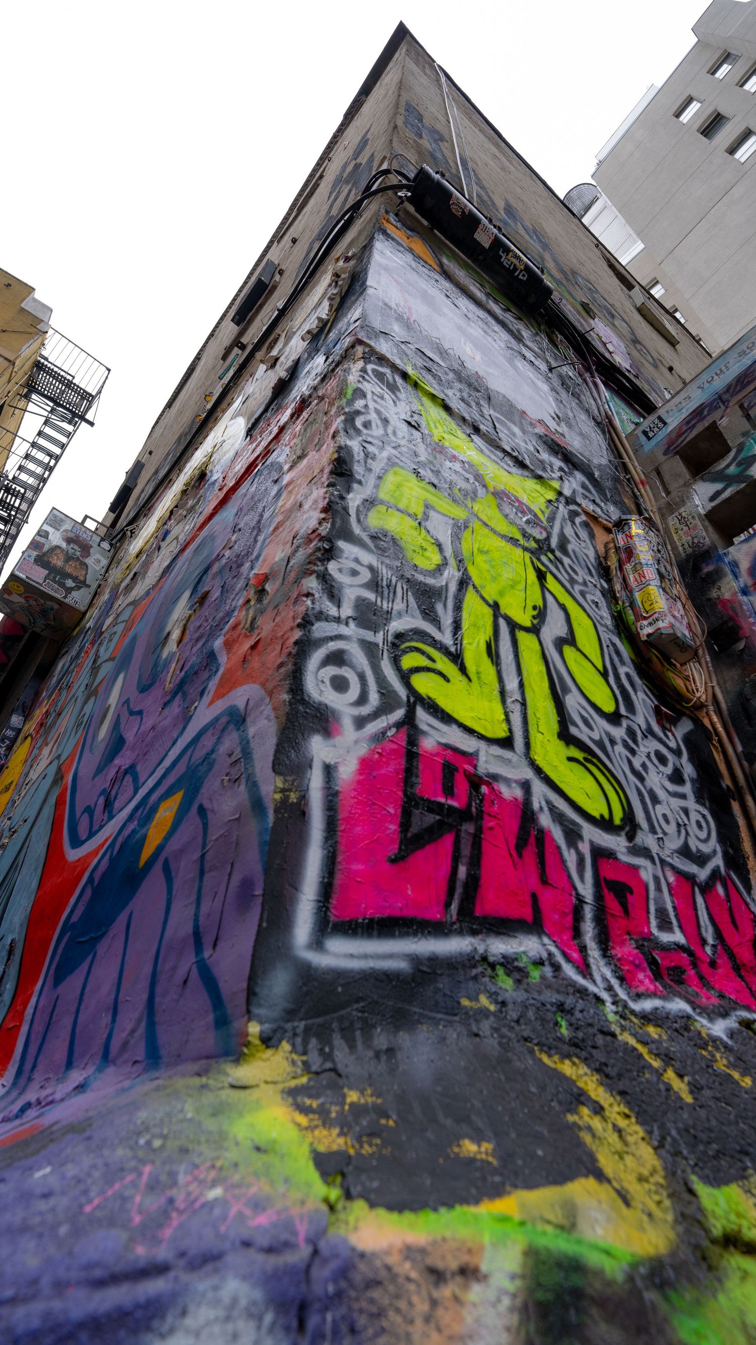 Graffiti-covered wall featuring bright pink and green spray paint designs.