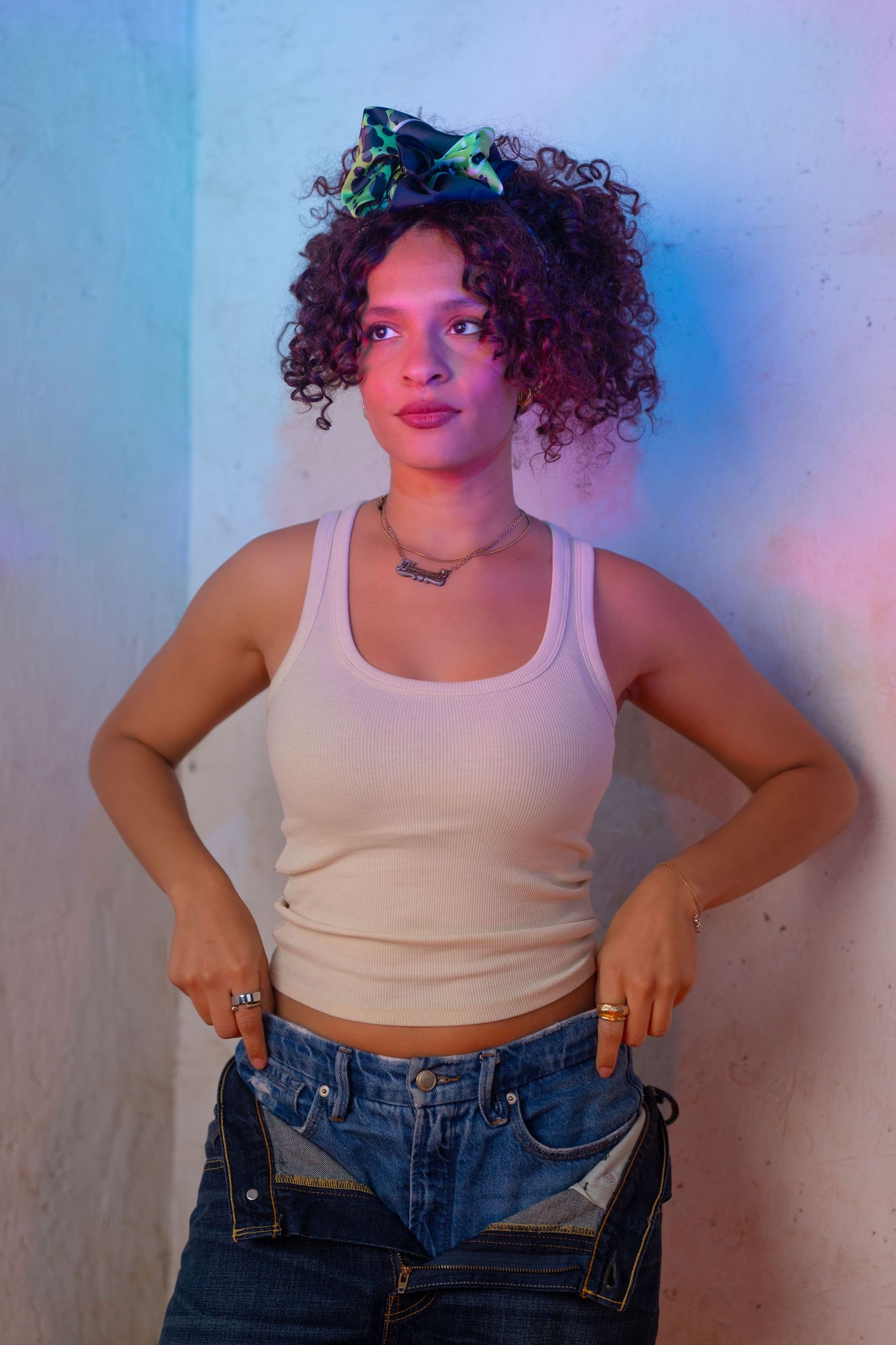 Person wearing a white crop top and jeans poses against a wall with blue and purple lighting effects.