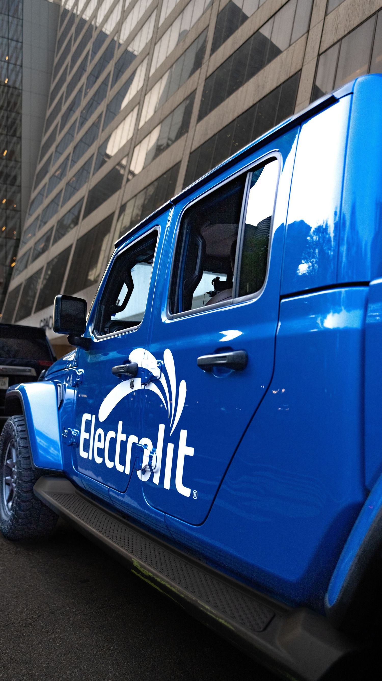 Side view of a bright blue branded vehicle with Electralit logo parked against modern architecture.