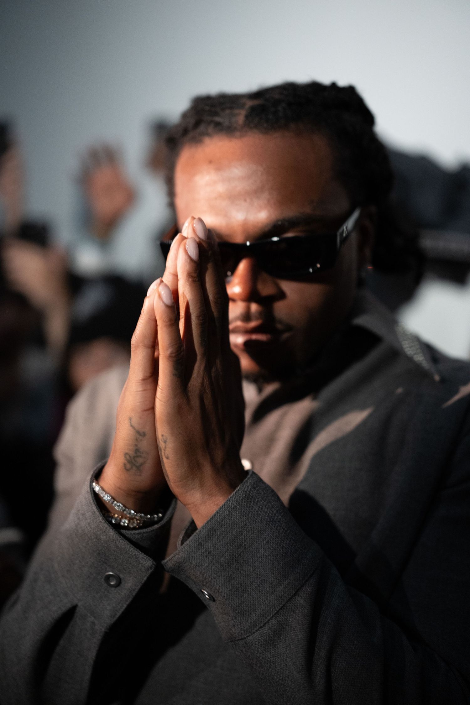 Artistic portrait of a performer in sunglasses with hands clasped in prayer position.