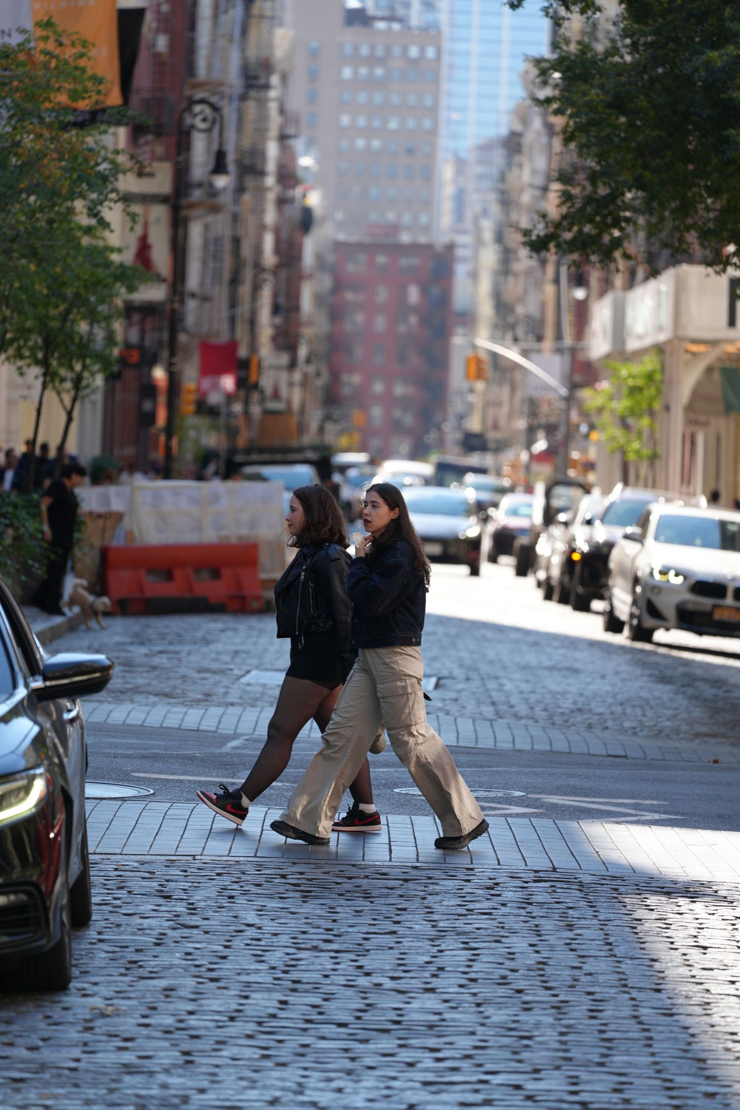 People walking on a sunlit cobblestone street in a city neighborhood.