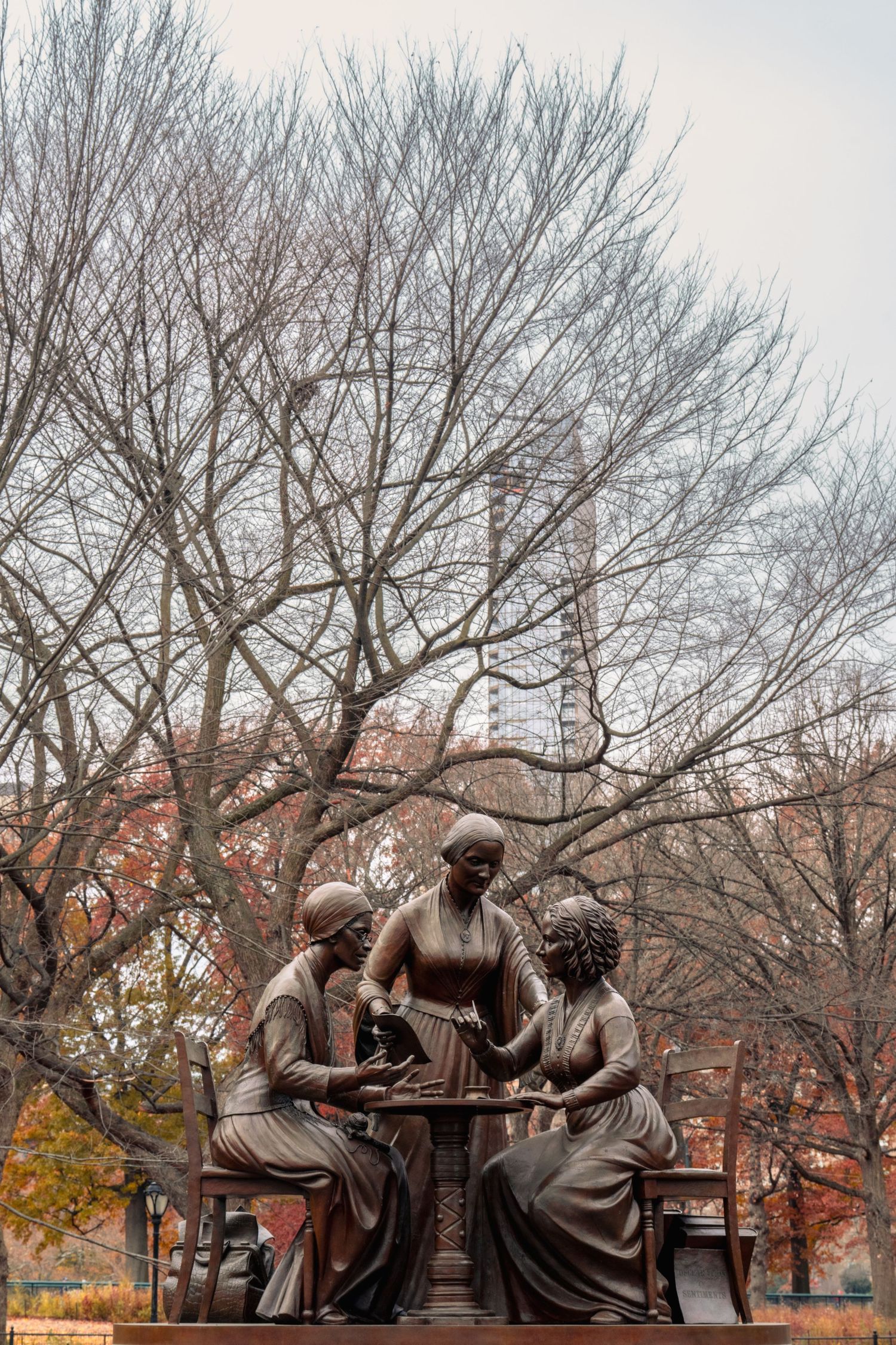 Bronze sculpture of figures seated on a bench under bare winter trees on a university campus.