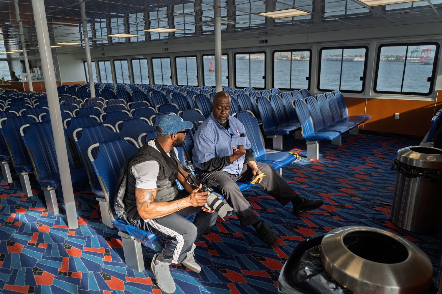 People seated in a modern airport terminal with blue and red patterned carpeting and large windows.