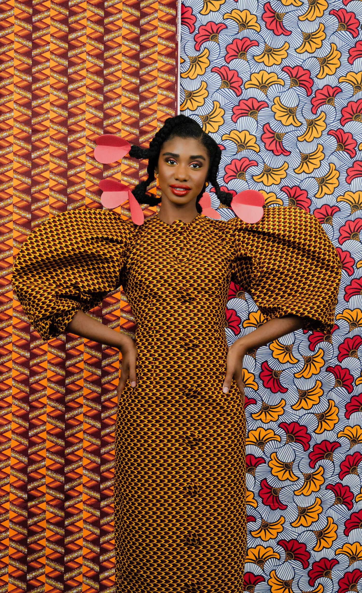 Model poses dynamically in African print dress against mixed pattern background.