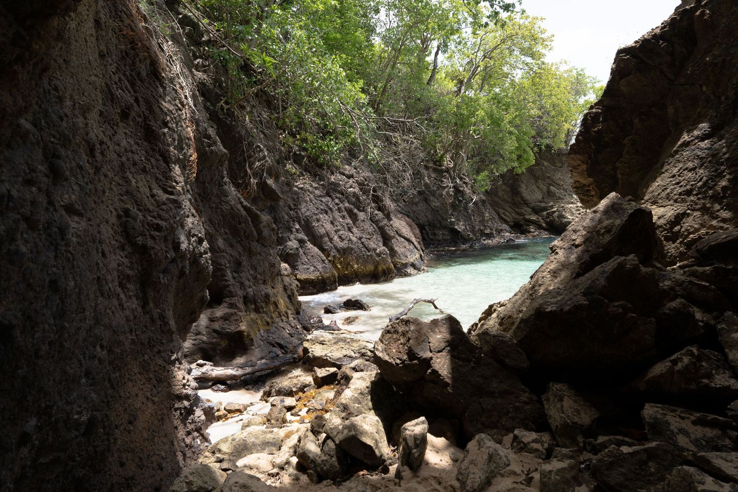 Rocky gorge with turquoise stream flowing between steep canyon walls and scattered boulders.