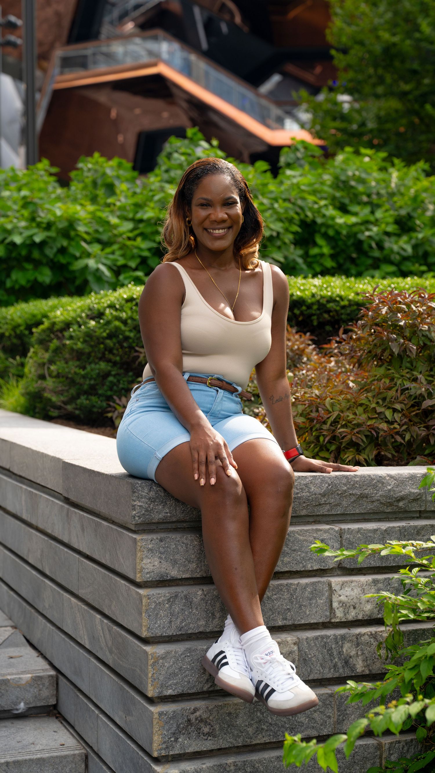 Person in casual summer attire relaxing on concrete steps surrounded by greenery.