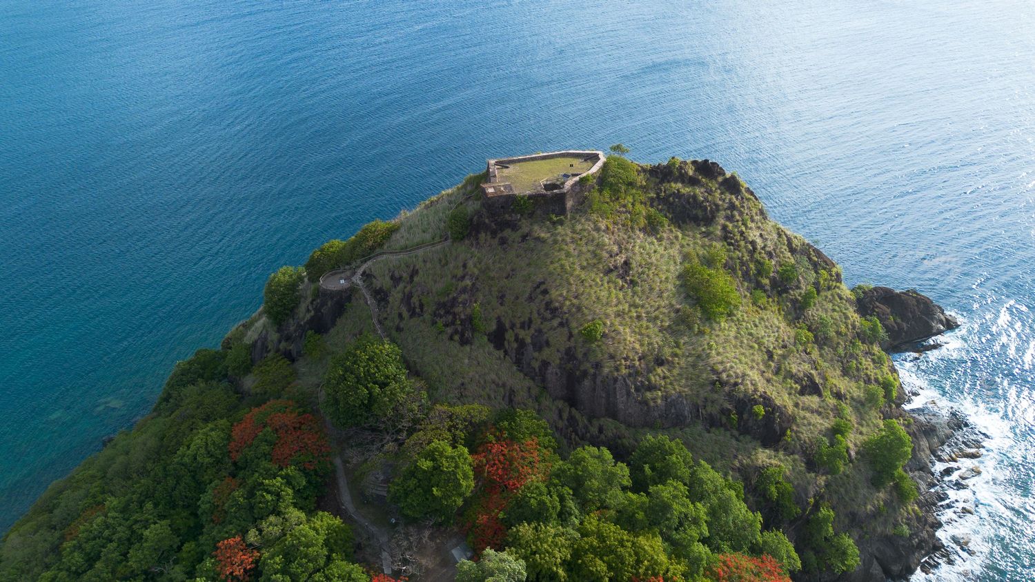 Aerial view of a rugged coastal headland with turquoise waters and steep cliffs.