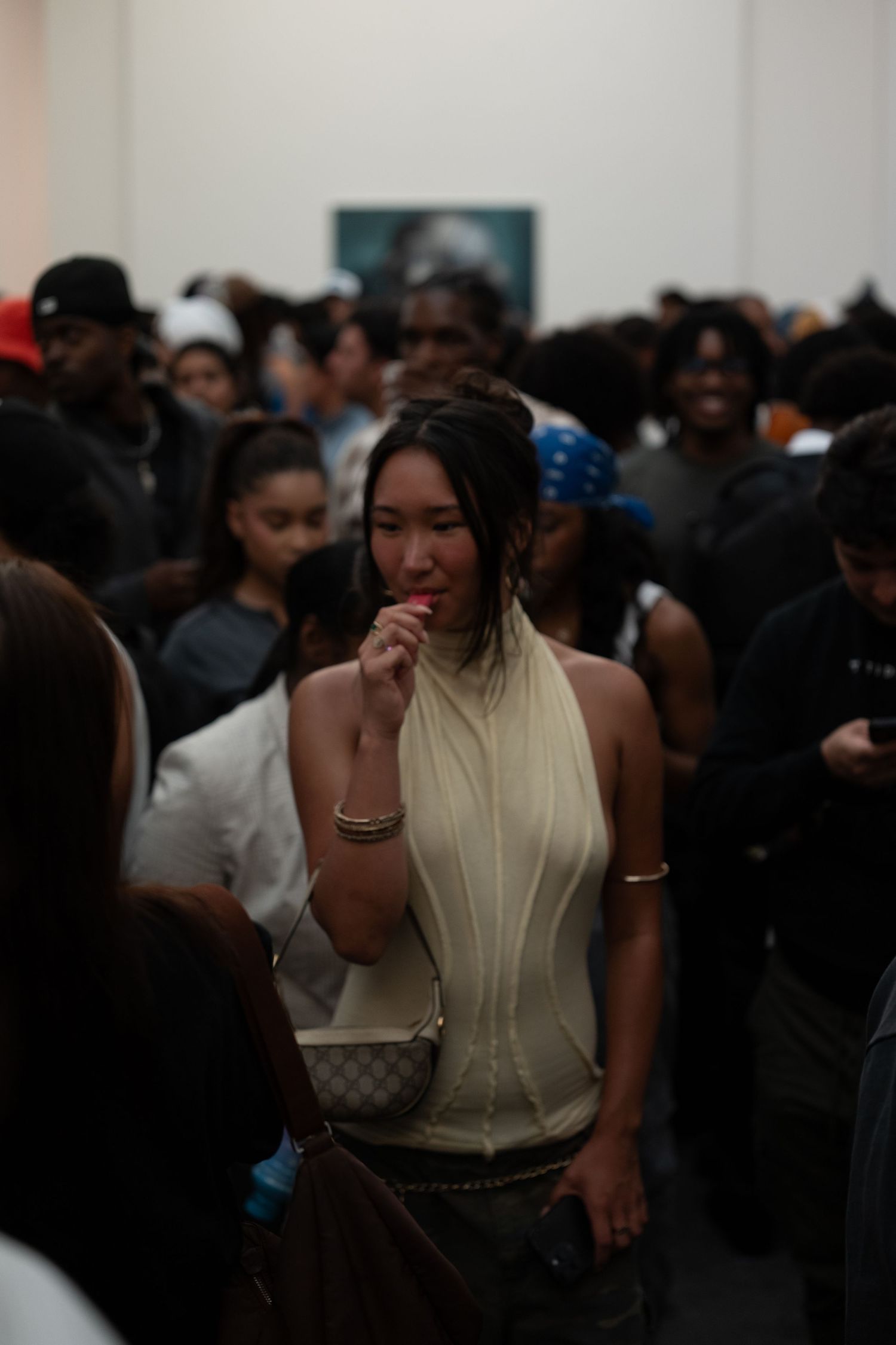 Crowd gathered in dimly lit gallery space with person in light colored top visible.