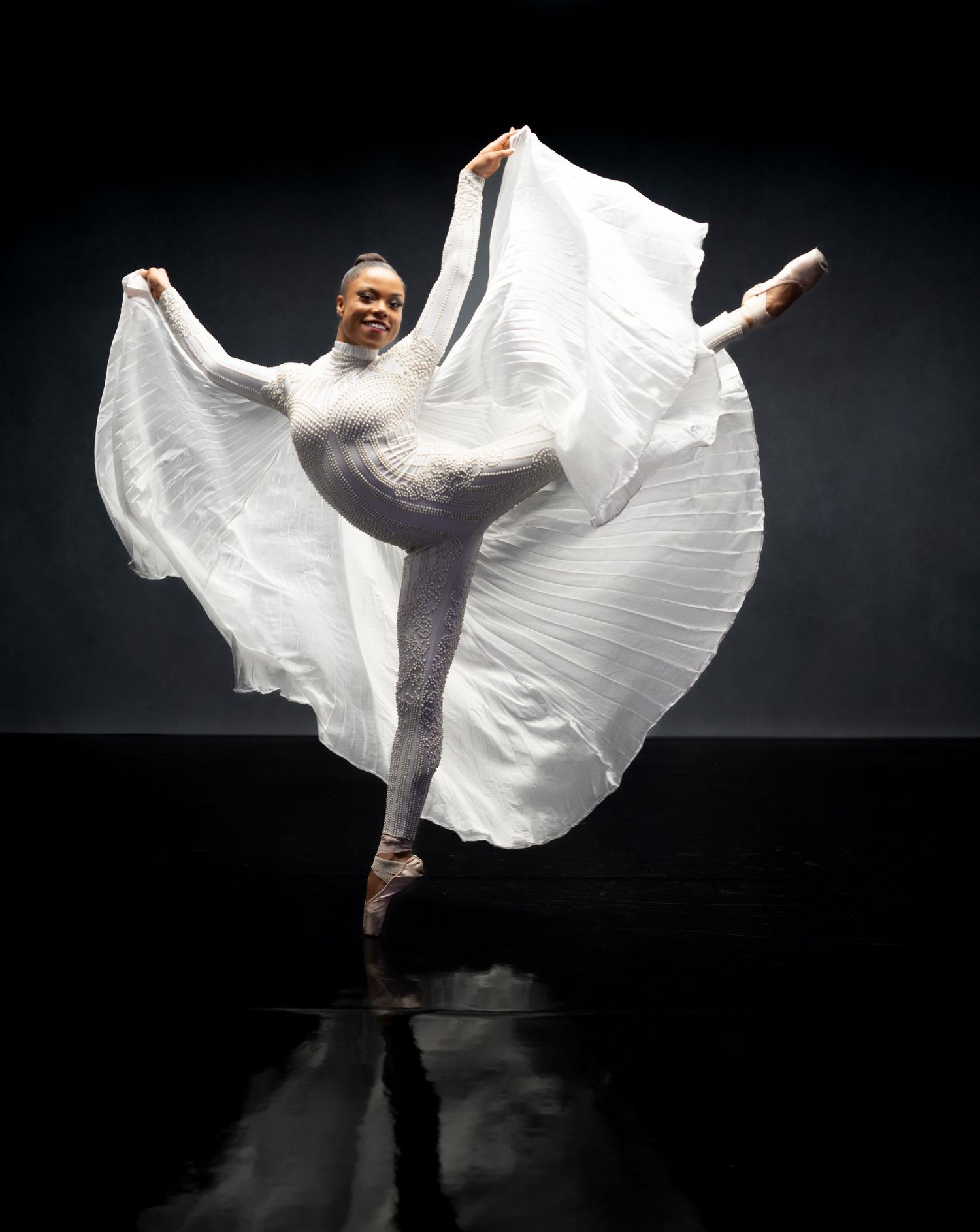 Modern dancer in white costume creates dramatic wing-like shapes with fabric against black backdrop.
