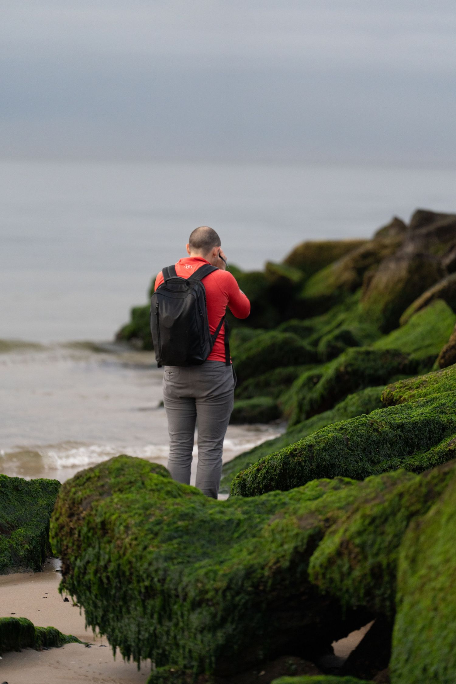 Person exploring moss-covered rocks along a rocky coastal shoreline.