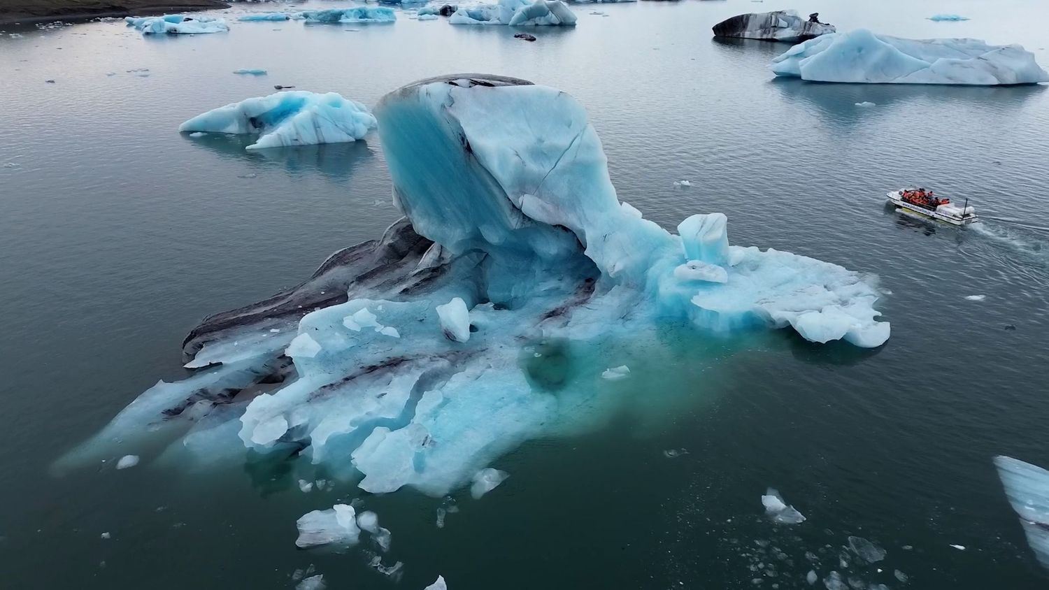 Massive blue icebergs floating in dark arctic waters with dramatic lighting and reflections.