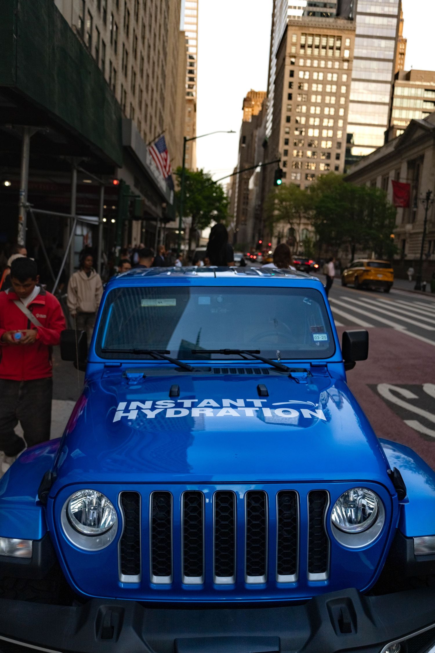 Front view of a bright blue Jeep with custom Hydration branding parked on a city street.