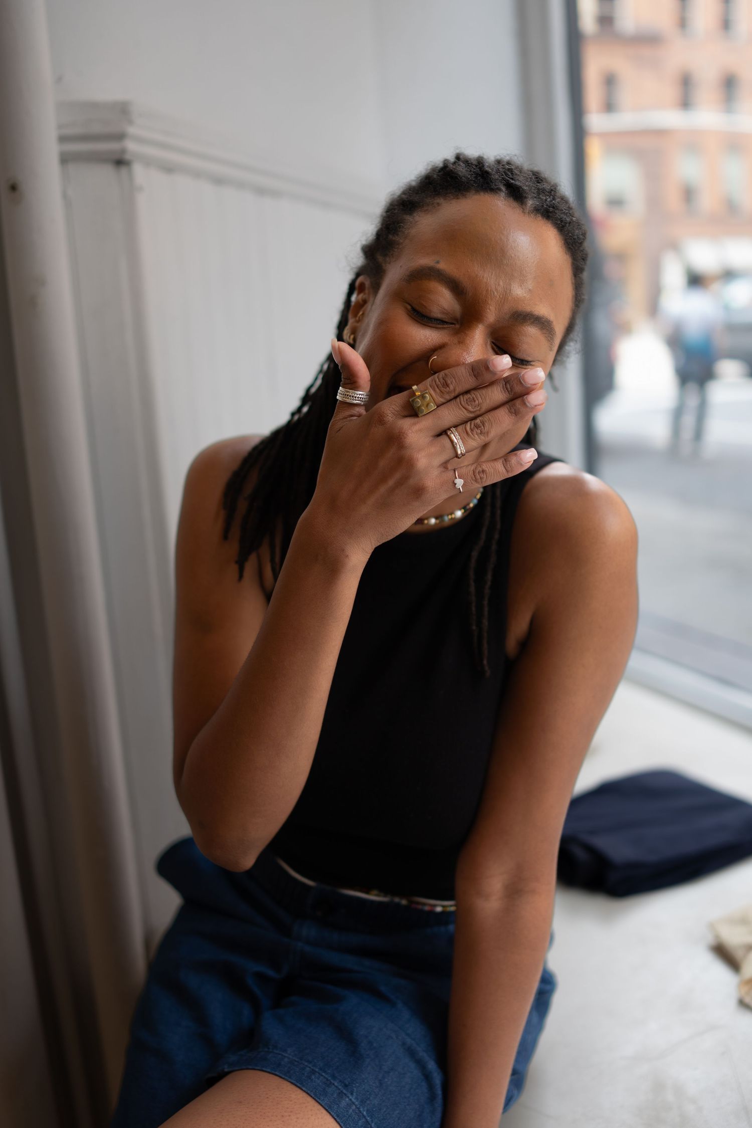 Person in dark clothing sitting by window with hands covering face in emotional moment.
