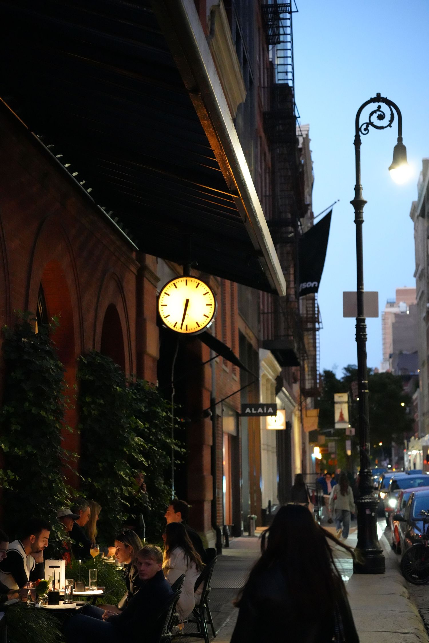 Illuminated city street at dusk with vintage clock and lampposts casting warm glow.