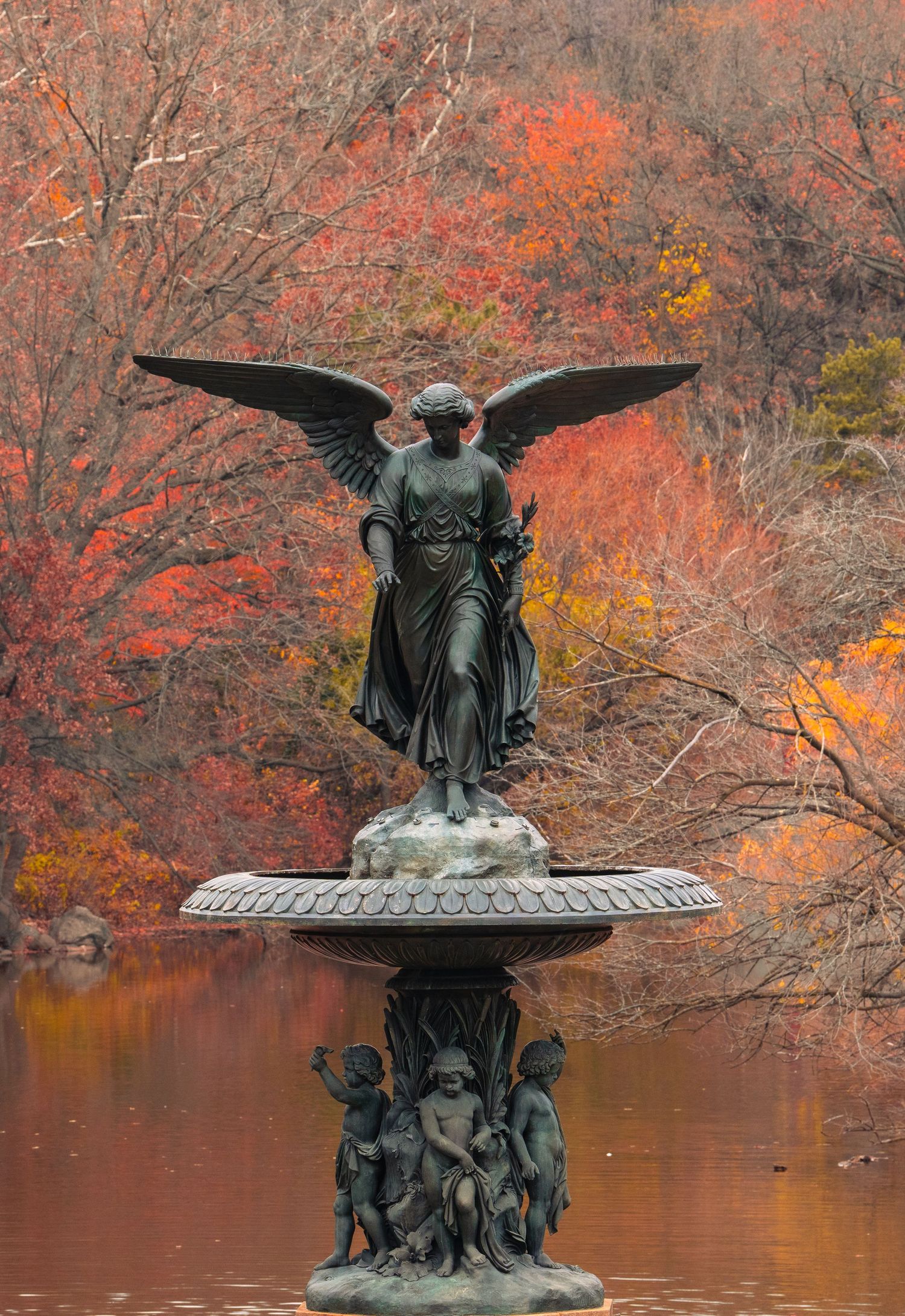 Bethesda Fountain angel statue surrounded by vibrant autumn foliage and reflective water in Central Park, New York City.