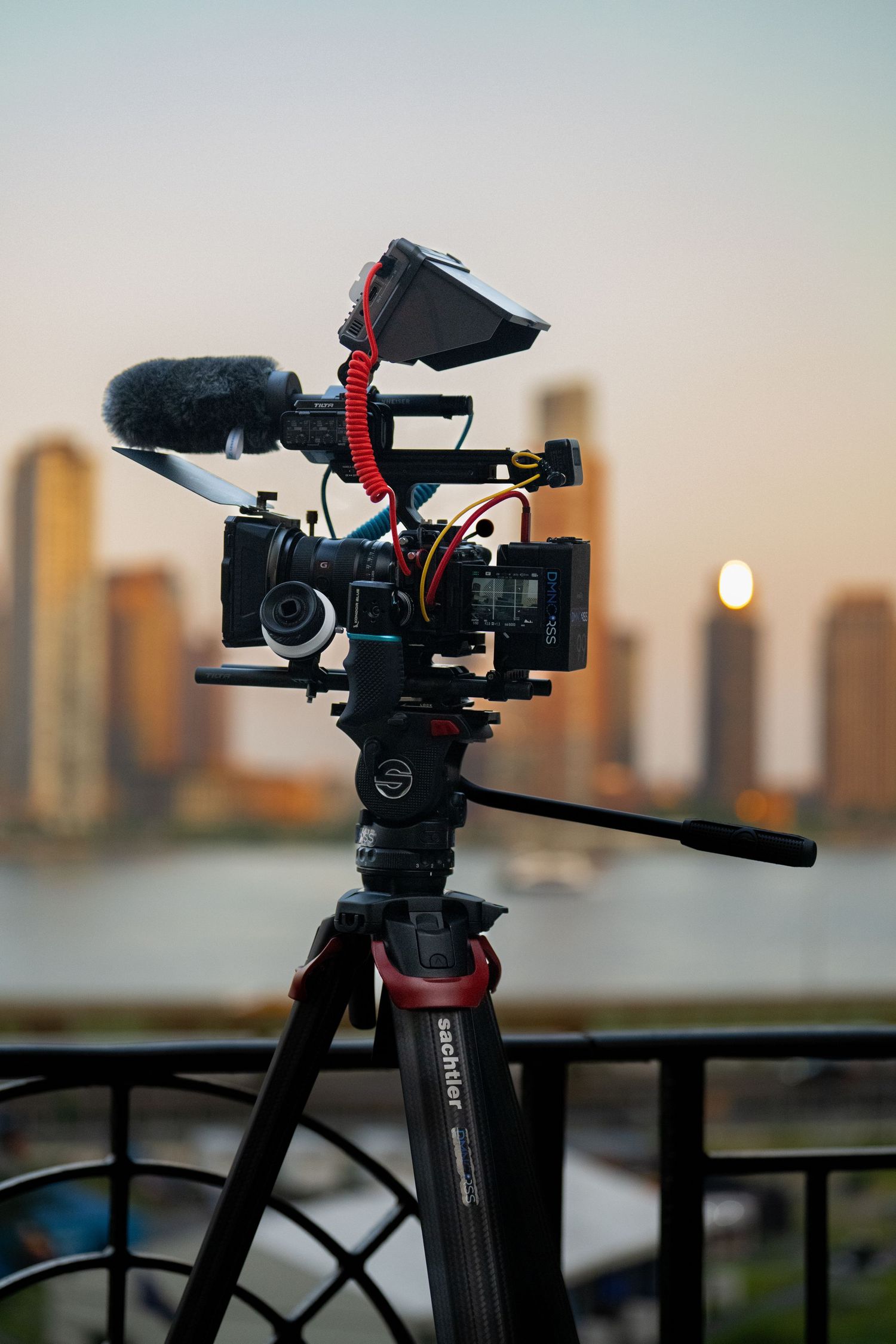 Video camera mounted on tripod capturing cityscape during golden hour.