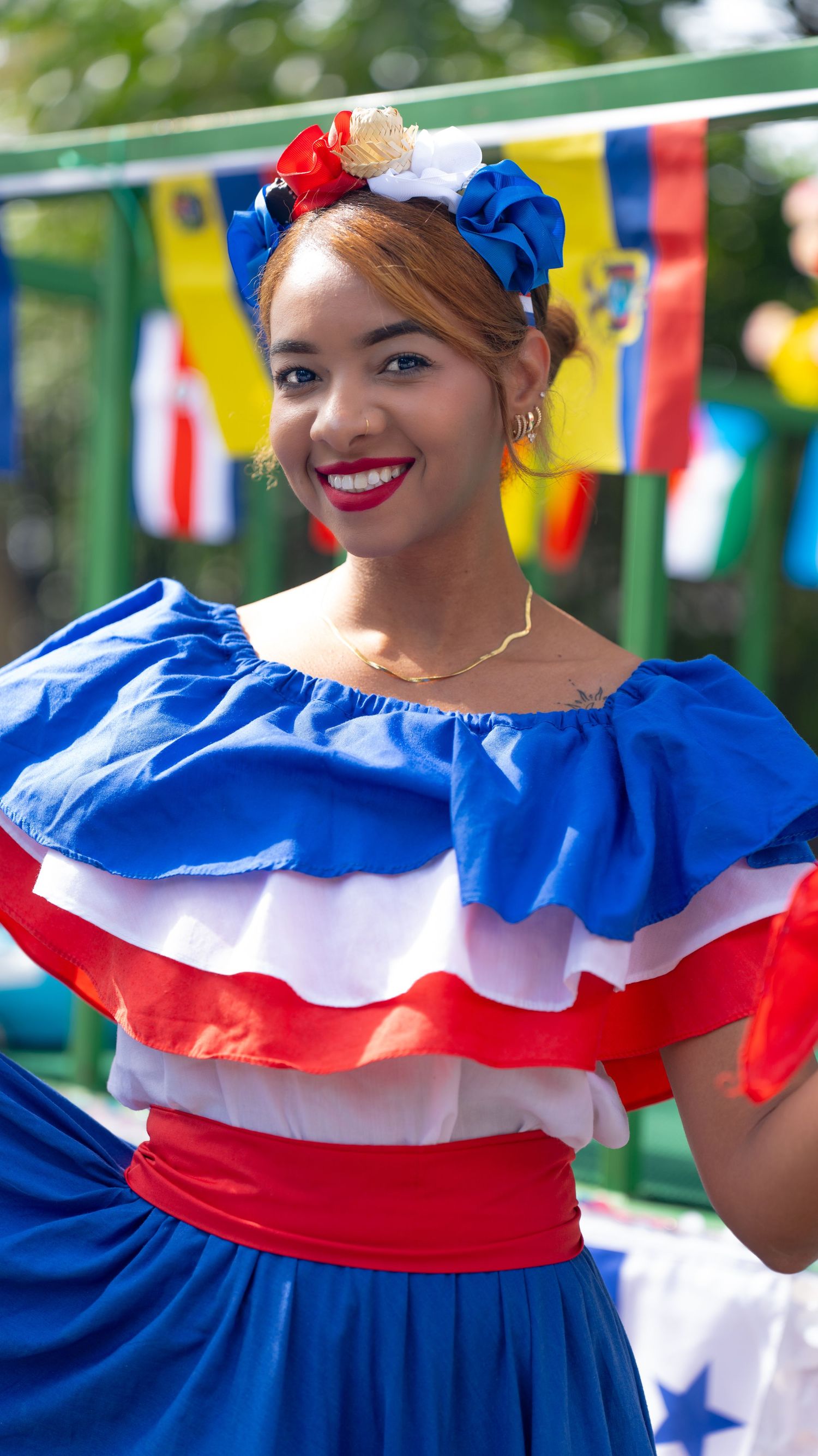 A traditional dancer wearing a blue, white and red ruffled dress performs near colorful flags.