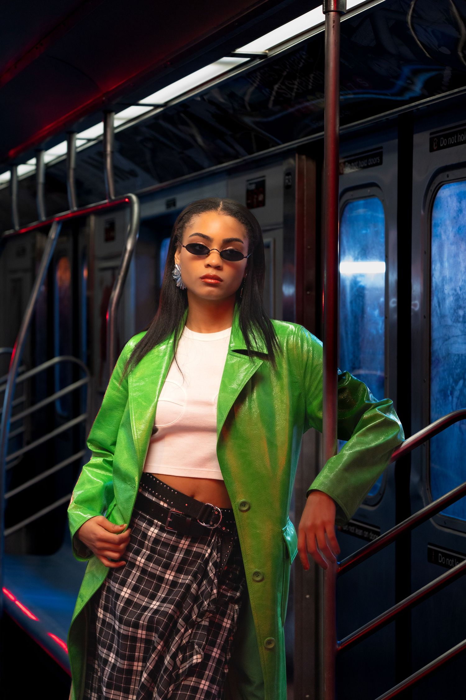 Fashion model in bright green jacket and plaid skirt posing in subway car setting.