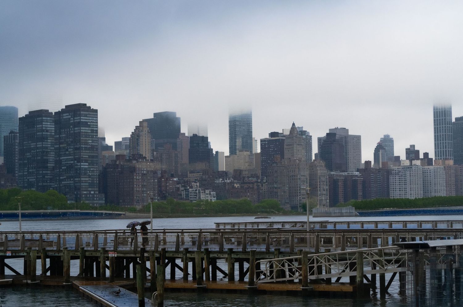 Cloudy skyline view of Manhattan from across the East River with a wooden pier in the foreground.