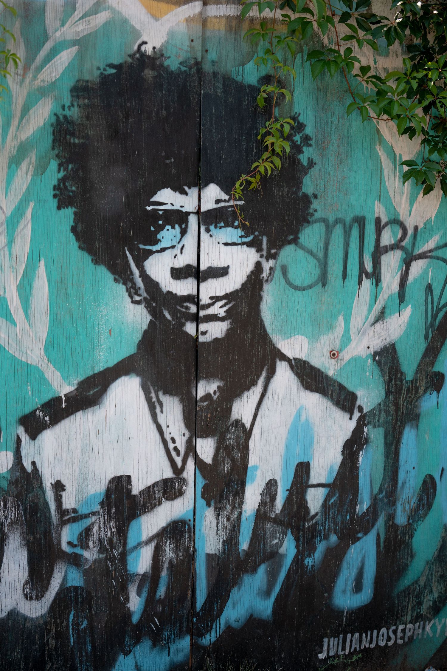 Black and white street art mural on turquoise wall showing silhouetted figures in an urban setting.