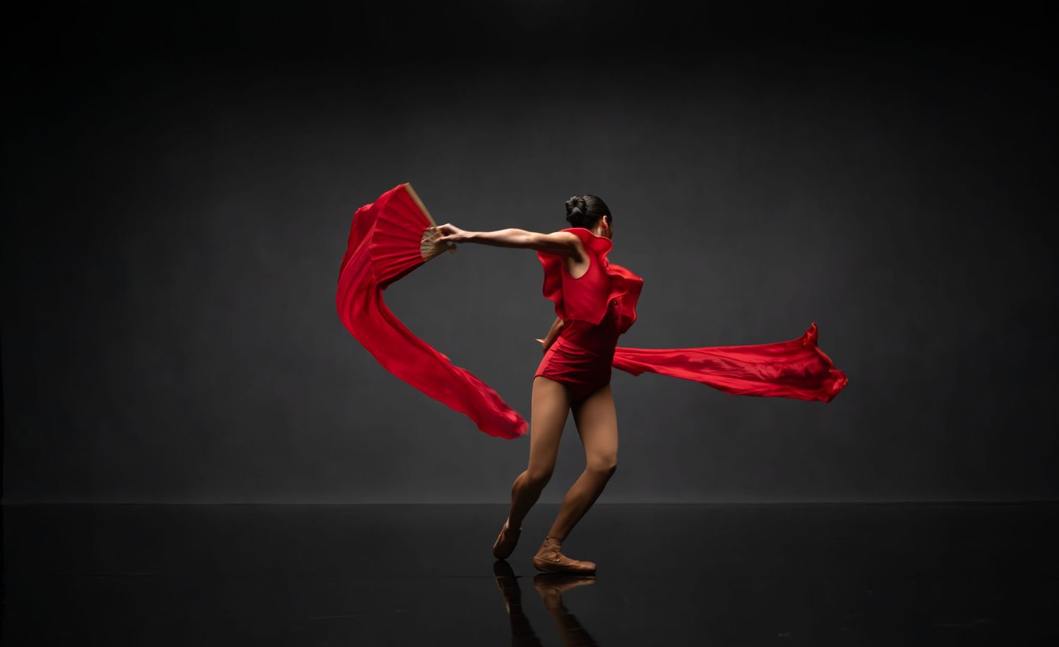 Dancer creates dynamic shapes with bright red fabric against dramatic dark background.