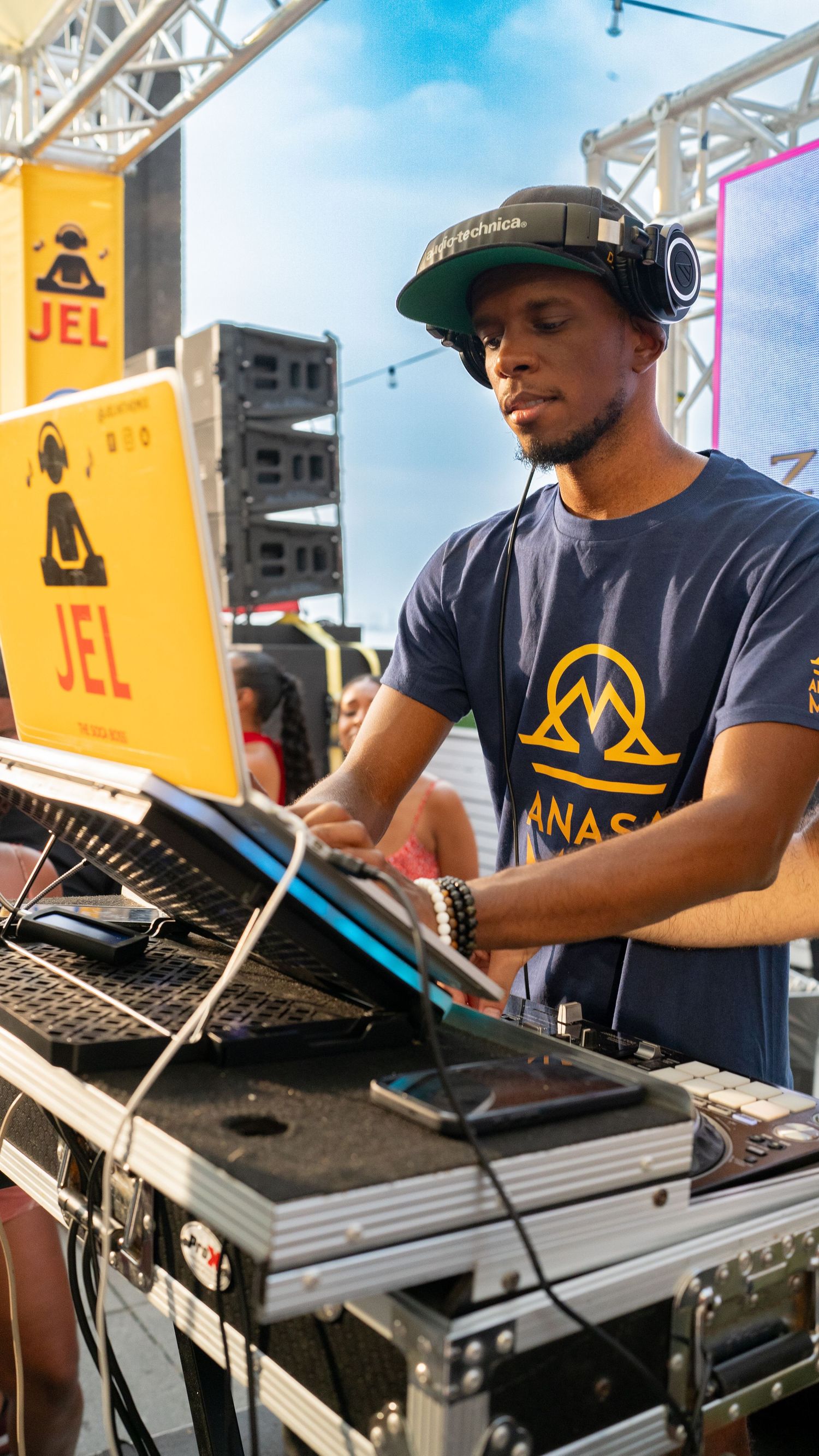 DJ performing at an outdoor festival with professional equipment and yellow JEL signage.