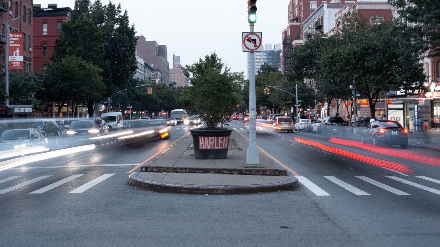 Wide panoramic view of an urban street intersection at dusk with light trails from passing cars.