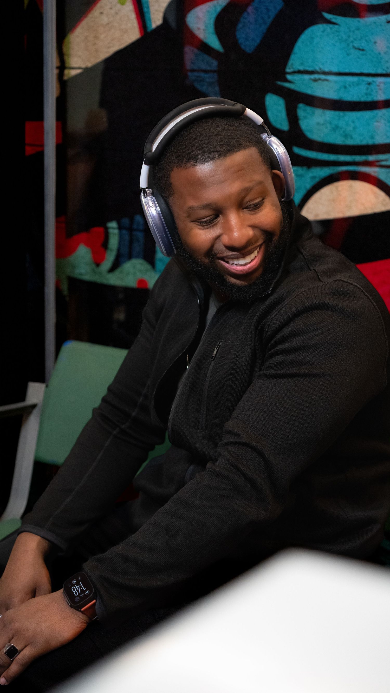 Person wearing headphones and black hoodie smiling while working in a colorful studio setting.