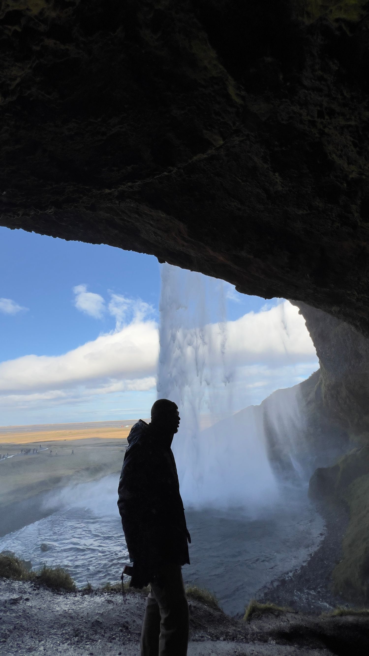 Silhouetted figure standing inside cave entrance with dramatic waterfall view.
