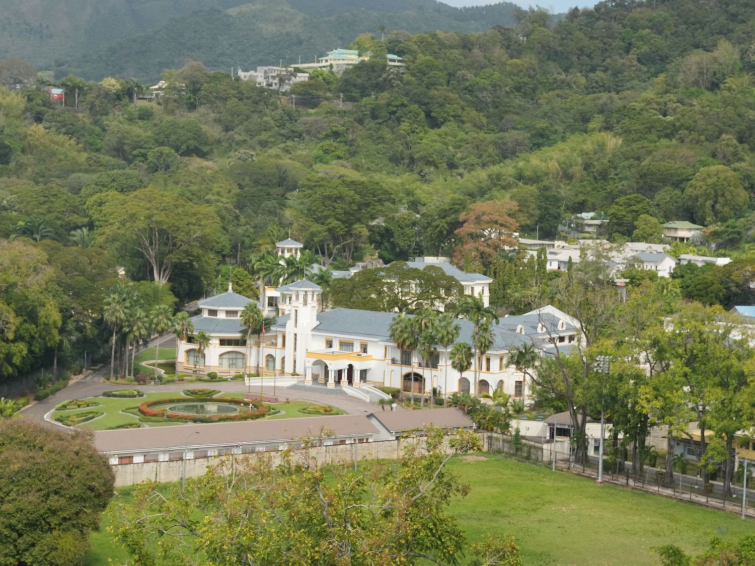 Aerial panoramic view of luxury hillside homes nestled among lush green tropical vegetation and mountains.