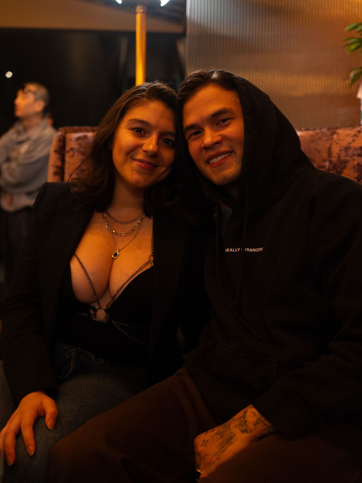 A smiling young couple poses together in a dimly lit lounge setting.