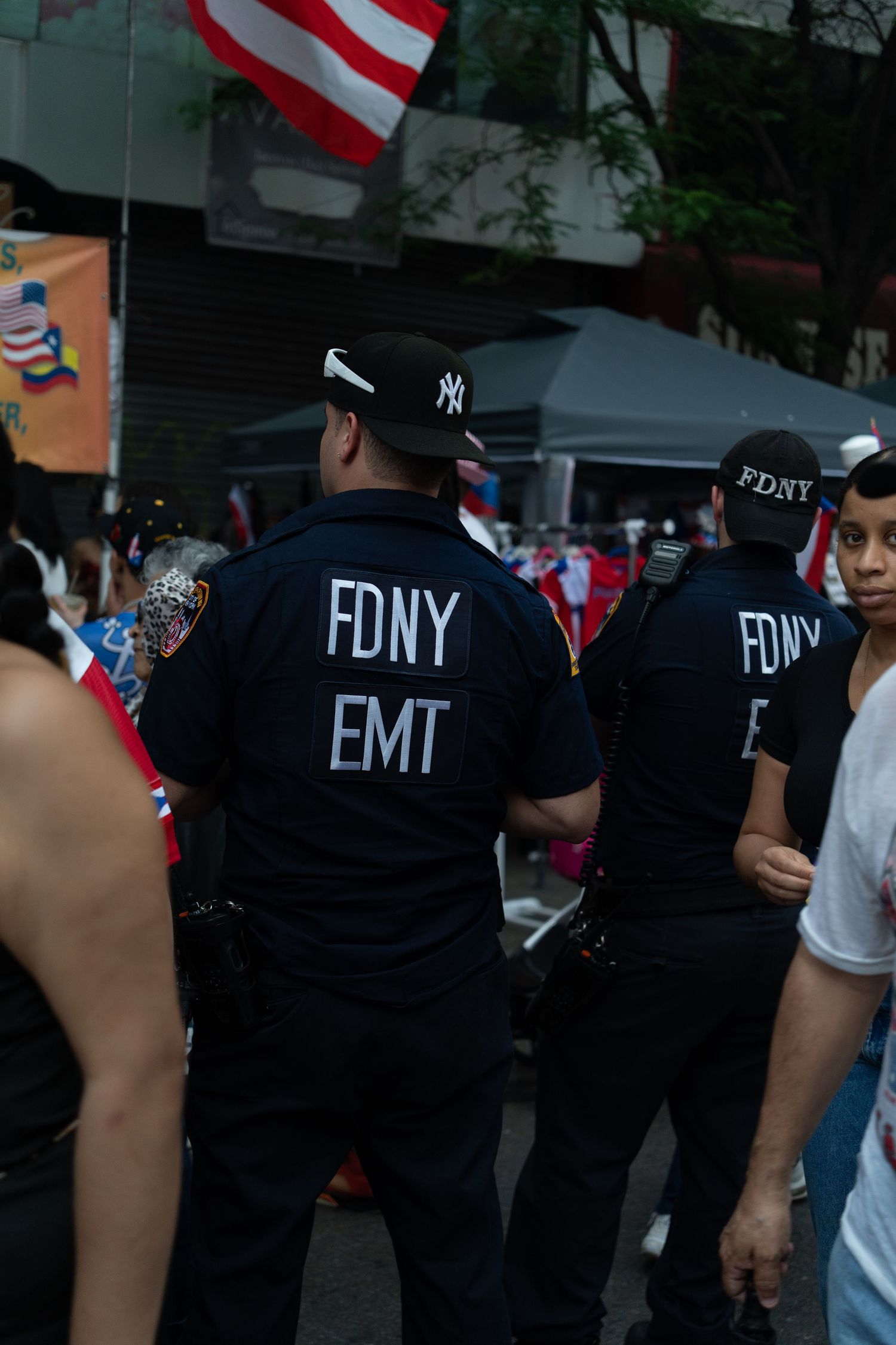FDNY and EMT personnel in black uniforms stand together during an event with American flags visible.