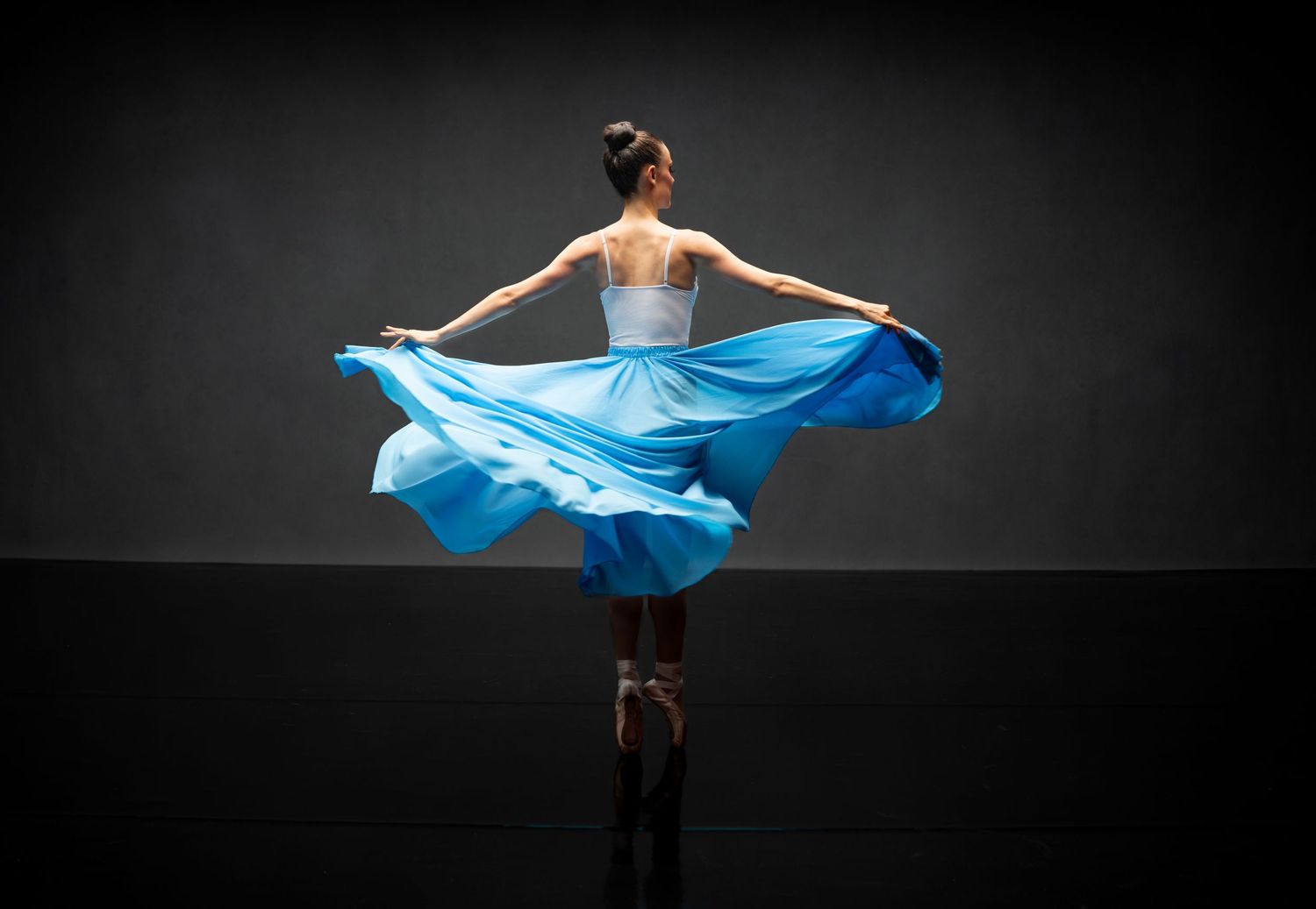 Dancer in light blue flowing fabric creates sweeping motion against dark background.