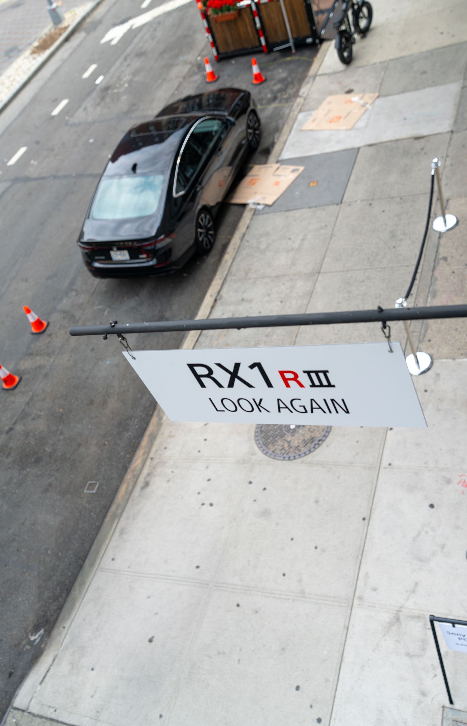 Aerial view of a street with cars and text reading 'RX7 RIII' and 'LOOK AGAIN' painted on pavement.
