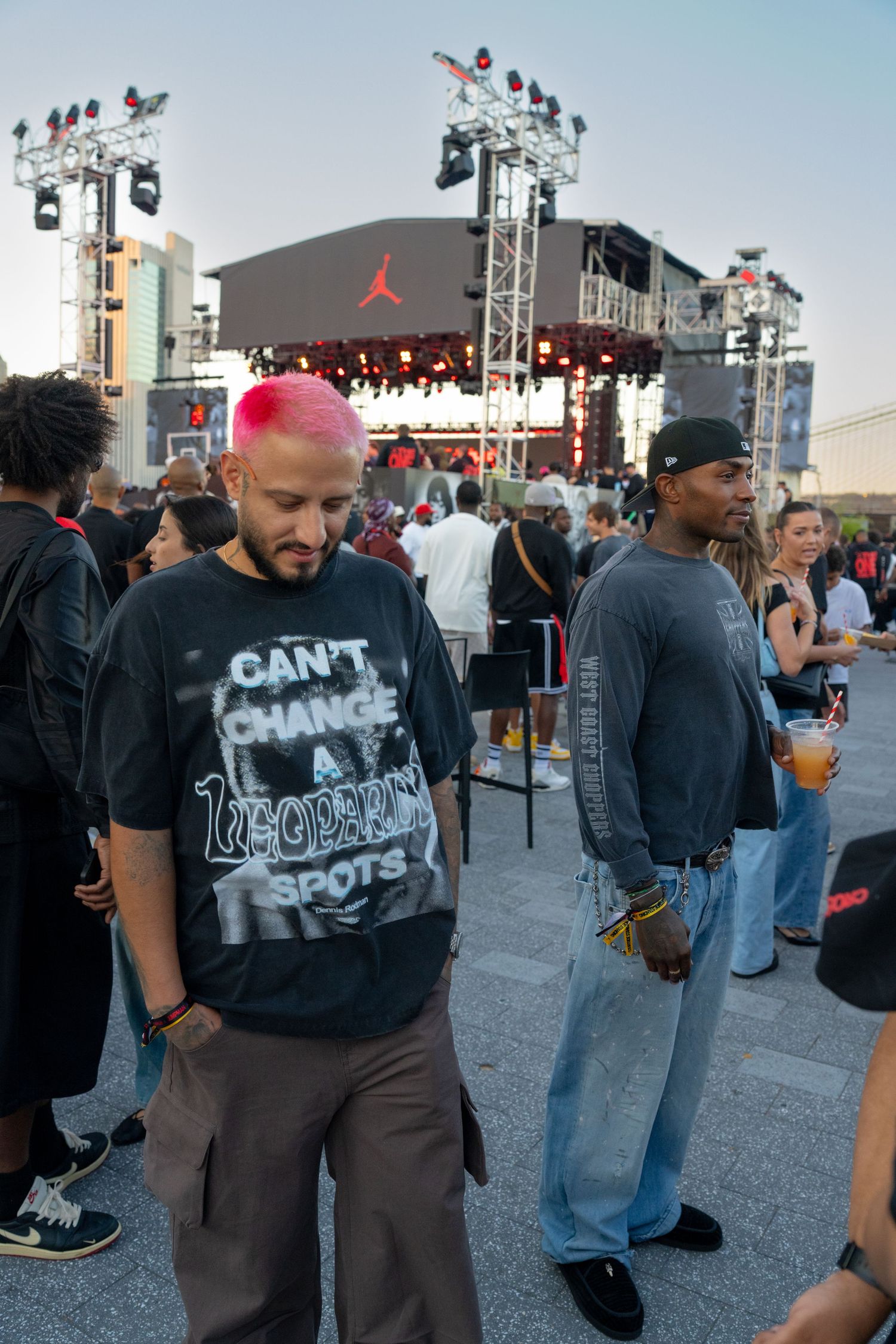 Crowd gathering at an outdoor urban event with stage lighting and equipment visible.