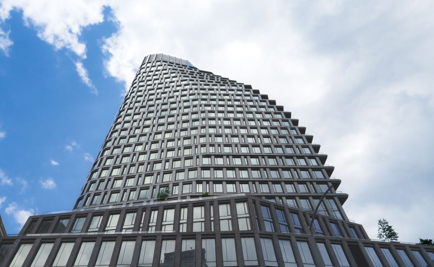 Modern glass office building with geometric facade patterns against blue sky with clouds.