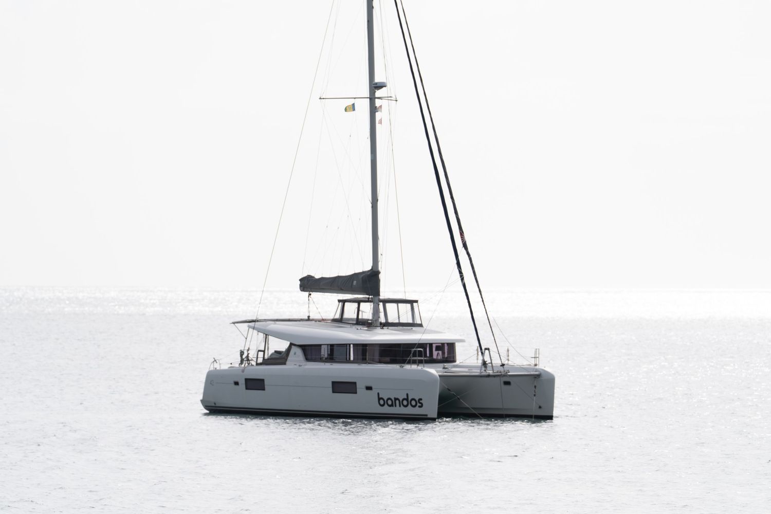 Large white catamaran yacht anchored in misty waters with mountains in the distance.
