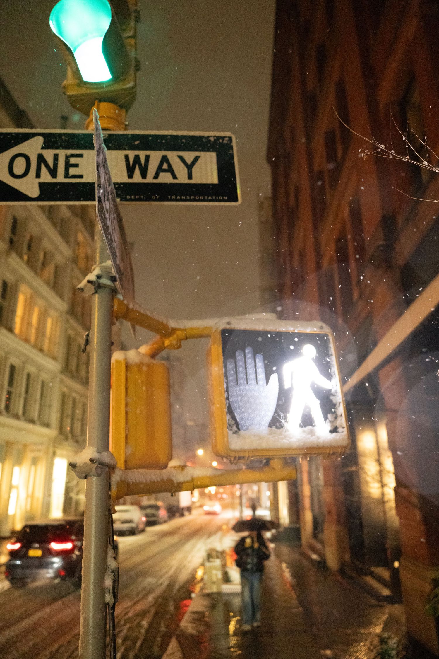 Snowy night street scene with glowing traffic light and one-way sign.