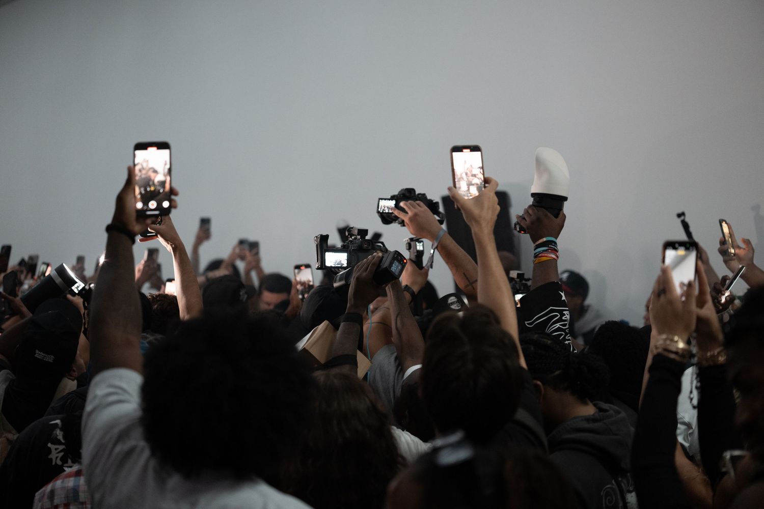 Silhouettes of people holding up phones and cameras in a dimly lit space.